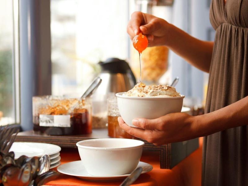 Osoba nabierająca płatki śniadaniowe z bufetu ze słoikami dżemu.