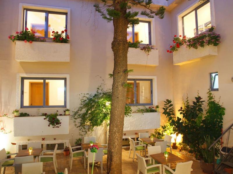 Patio hotelowy z stołami, krzesłami, roślinami i dużym drzewem na środku.