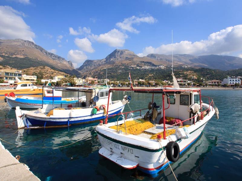 Kolorowe łodzie rybackie zacumowane w spokojnym porcie pod częściowo pochmurnym niebem.