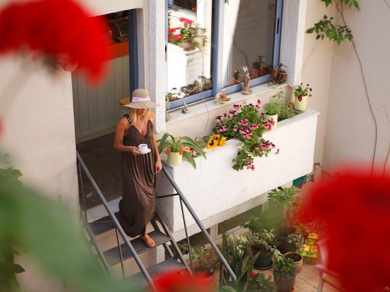 Kobieta w brązowej sukience schodzi po schodach domu z kwiatami na oknach.