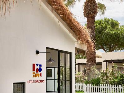 Biały domek letniskowy ze strzechą, szklanymi drzwiami przesuwnymi i palmami w ogrodzie