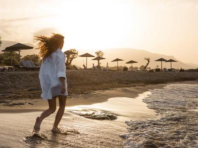 Kobieta chodzi boso po wodzie na plaży o zachodzie słońca.