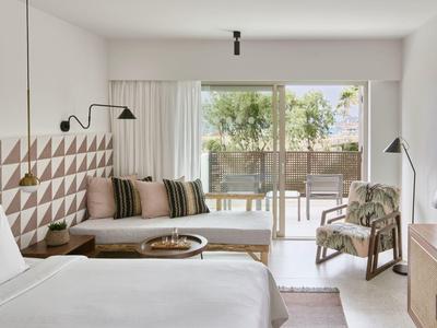 Jasny pokój hotelowy z łóżkiem podwójnym, geometryczną dekoracją ściany i tarasem z widokiem na ogród.