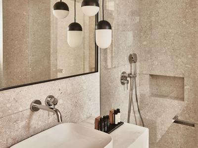 Modernes Badezimmer mit großem Spiegel, hängenden Lampen, rechteckigem Waschbecken und beiger Marmoroptik.