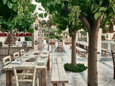 Outdoor-Restaurant mit Holztischen, Bänken, Stühlen und Bäumen auf gepflastertem Boden.