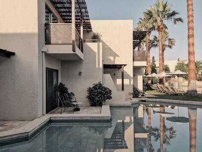 Moderner Wohnhaus-Komplex mit Pool, Palmen und klaren Linien, bei klarem Himmel.