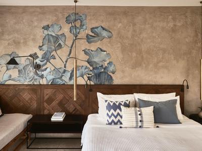 Schlafzimmer mit Holzkopfteil, Blumenwandmalerei und weißen Bettdecken mit Kissen.
