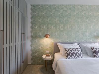 Modernes Schlafzimmer mit grün gemusterter Wand, grauem Schrank, weißem Bett und Nachttischlampe.