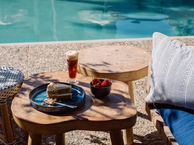 Piccolo tavolo di legno vicino alla piscina con bevanda, snack e zona salotto con cuscini