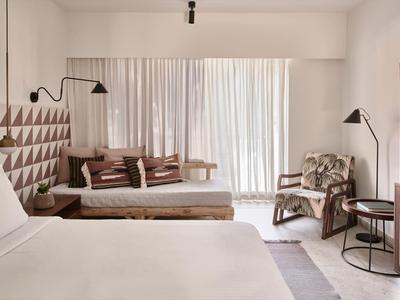 Jasny pokój hotelowy z łóżkiem podwójnym, sofą, fotelem i dużym oknem z zasłonami.