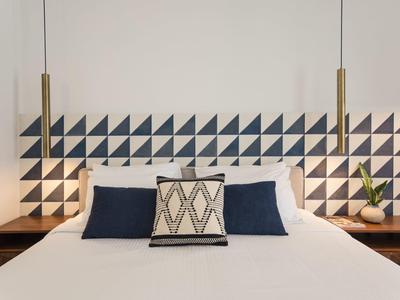 Modernes Hotelzimmer mit weißem Bett, geometrischem Kopfteil und minimalistischer Dekoration.