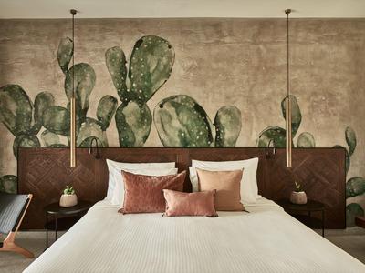 Schlafzimmer mit großem Bett, Kaktus-Wandbild und Hängelampen auf beiden Seiten.