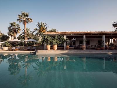 Piscina dell'hotel con sedie a sdraio, palme e area salotto ombreggiata sotto un cielo sereno.