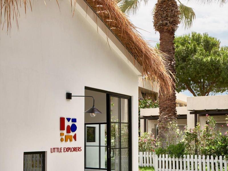 Biały domek letniskowy ze strzechą, szklanymi drzwiami przesuwnymi i palmami w ogrodzie