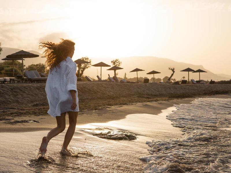 Kobieta chodzi boso po wodzie na plaży o zachodzie słońca.