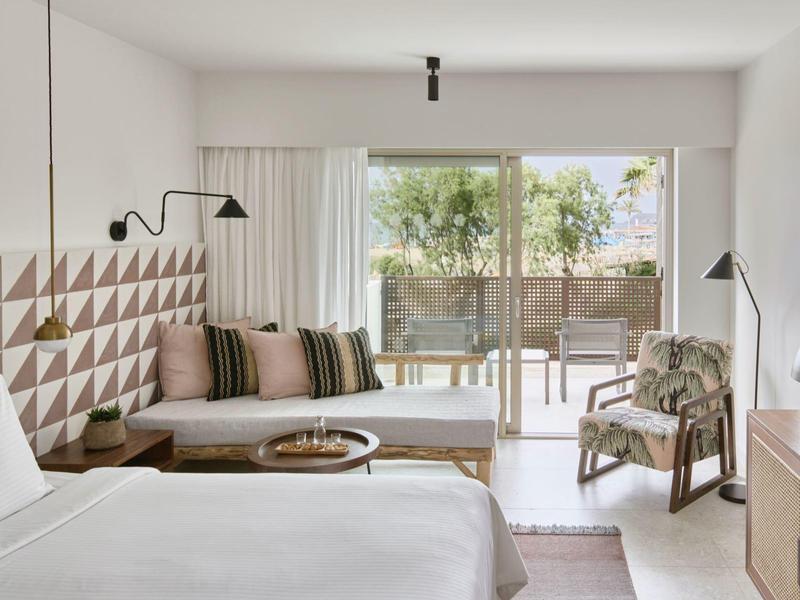 Jasny pokój hotelowy z łóżkiem podwójnym, geometryczną dekoracją ściany i tarasem z widokiem na ogród.