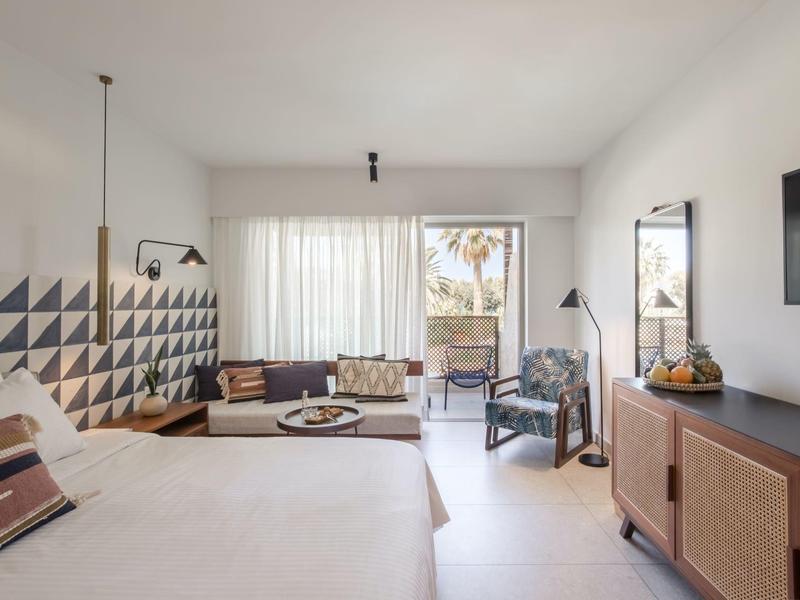 Helles Hotelzimmer mit großem Bett, Sofa, Sesseln und TV an der Wand.