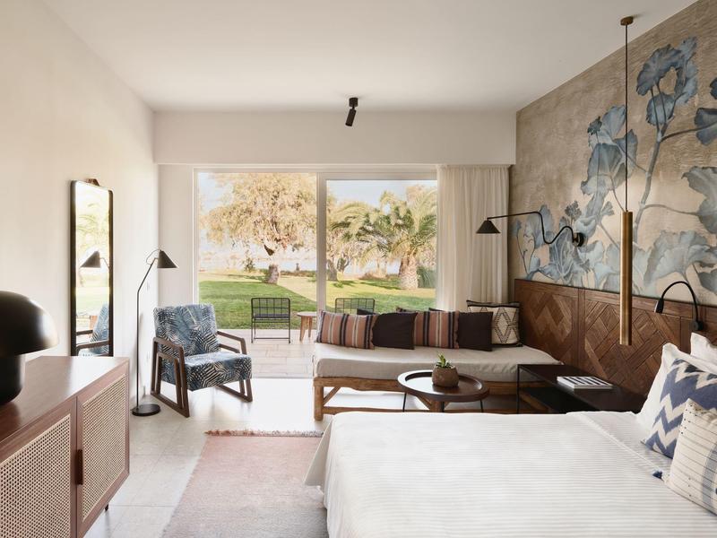 Nowoczesny pokój hotelowy z łóżkiem, sofą, dużym muralem ściennym i widokiem na ogród przez przeszklone przesuwne drzwi.