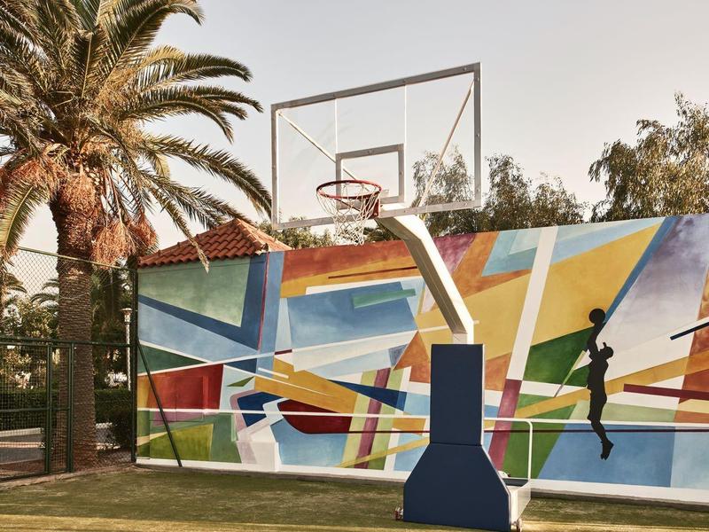 Kolorowy plac do koszykówki z koszem, palmami i geometrycznym muralem.