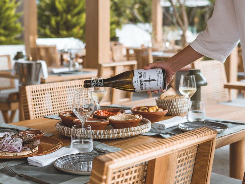 Kelner nalewający wino przy stole nakrytym jedzeniem na zewnątrz restauracji.