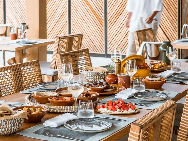 Nakryty drewniany stół z daniami śniadaniowymi w jasnej restauracji z wiklinowymi krzesłami.