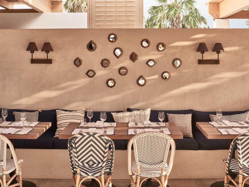 Przytulna przestrzeń z krzesłami, stołami i dekoracyjną ścianą w ciepłych tonacjach.