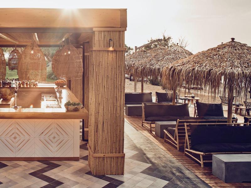 Strefa na zewnątrz ośrodka z leżakami plażowymi i barem pod parasolami ze słomy.