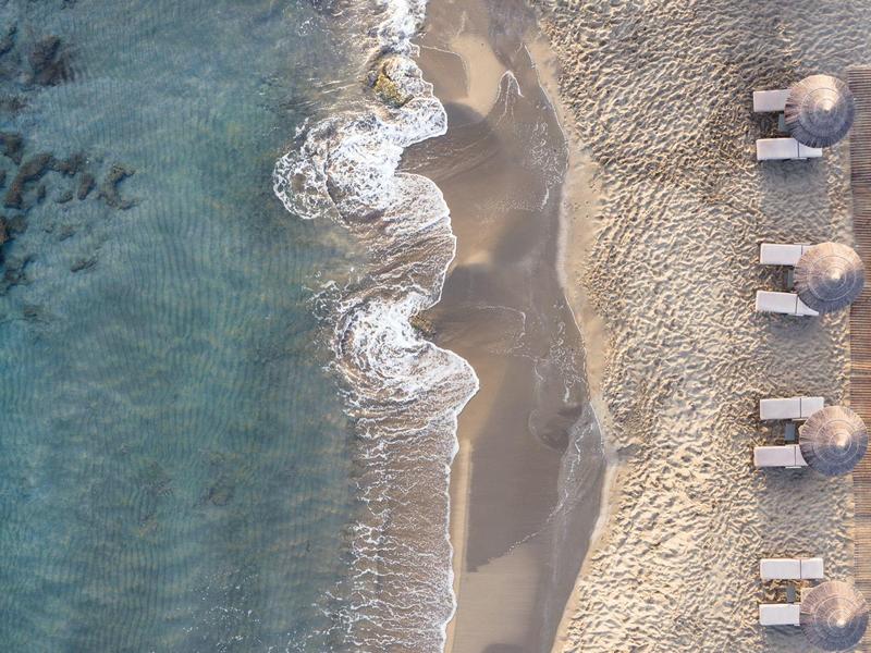 Zdjęcie z lotu ptaka plaży z małymi parasolami i falami przy brzegu.