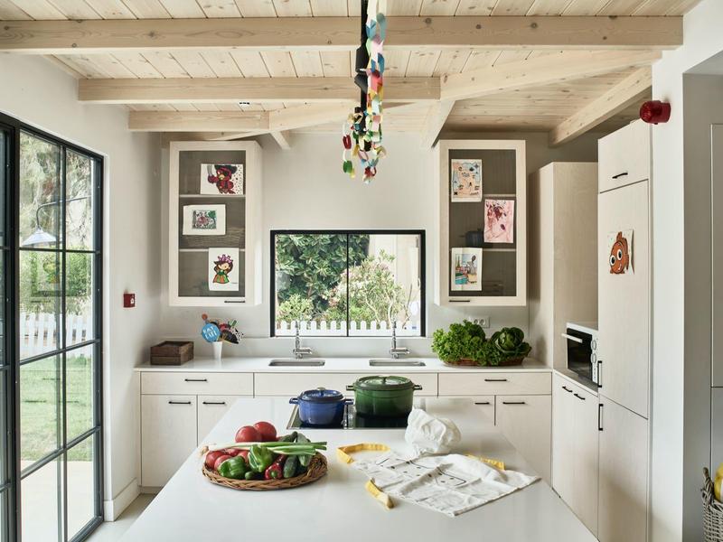 Jasna, nowoczesna kuchnia z wyspą, drewnianymi belkami i dużym oknem z widokiem na ogród.