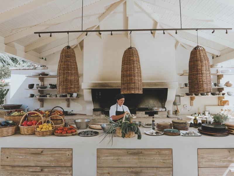 Otwarta kuchnia z drewnianymi panelami, wiszącymi lampami i kucharzem przed dużym kominkiem.