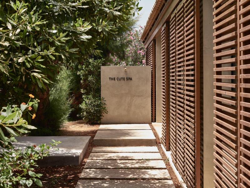 Nowoczesny korytarz hotelowy z drewnianymi żaluzjami i bujną zielenią wzdłuż ścieżki.