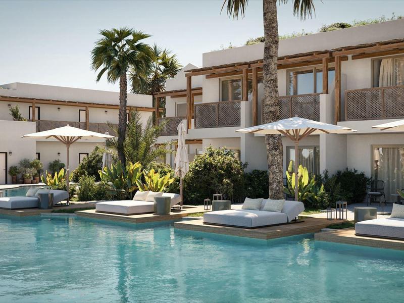 Nowoczesny basen hotelowy z leżakami i parasolami obok dwupiętrowych białych budynków i palm.