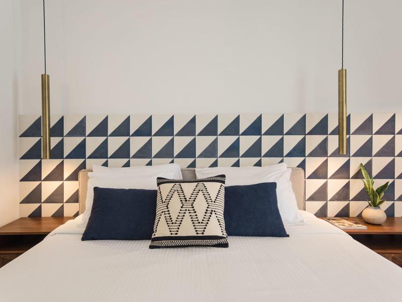 Modernes Hotelzimmer mit weißem Bett, geometrischem Kopfteil und minimalistischer Dekoration.