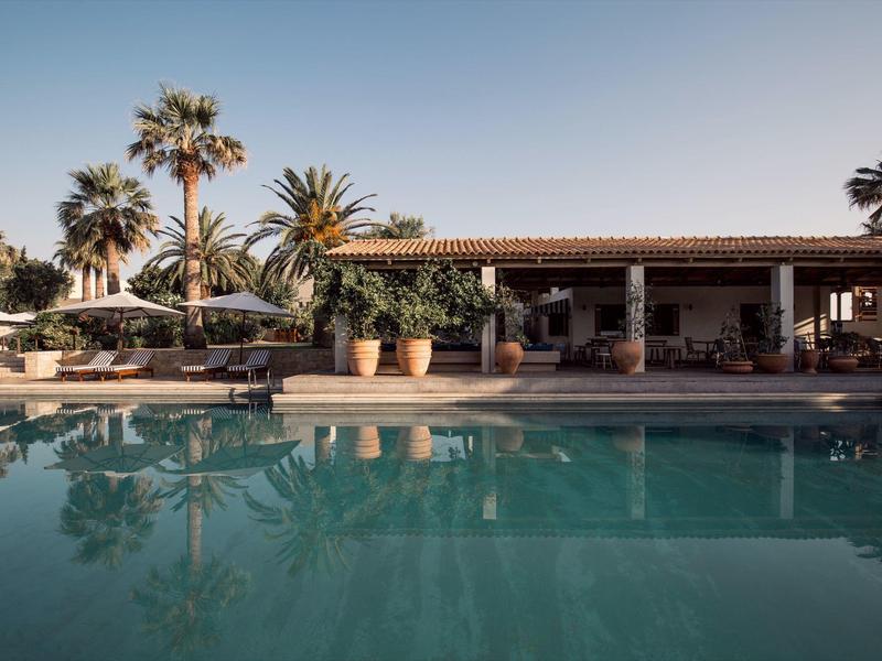 Hotelpool mit Sonnenliegen und Palmen bei klarem Himmel