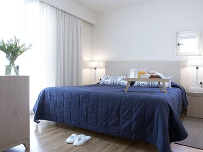 Helles Schlafzimmer mit großem Bett, blauem Bettbezug, Nachttischen und weißen Wänden.