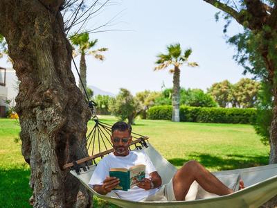 Man leest ontspannen een boek in een hangmat tussen bomen in een park.