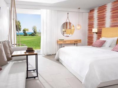 Helles Schlafzimmer mit großem Fenster, Doppelbett, Sofa, Tisch und Meerblick im Hintergrund.