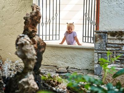 Een klein meisje leunt op een vensterbank en kijkt in een tuin met een sculptuur.