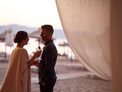 Coppia che brinda con una bevanda sulla spiaggia al tramonto.