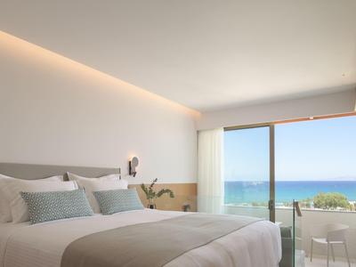 Helles Schlafzimmer mit modernem Bett, großem Fenster und Blick auf Meer und Terrasse.