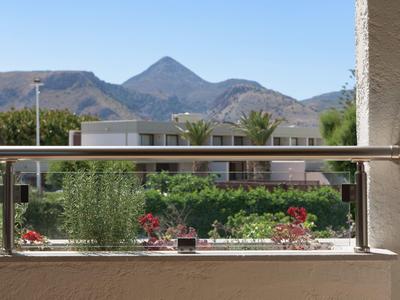 Uitzicht vanaf balkon op een tuin met bloemen en bergen op de achtergrond bij heldere lucht.