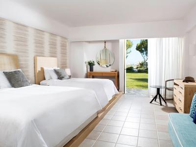 Modern eingerichtetes Hotelzimmer mit zwei Betten, Schreibtisch und Blick auf den Garten.