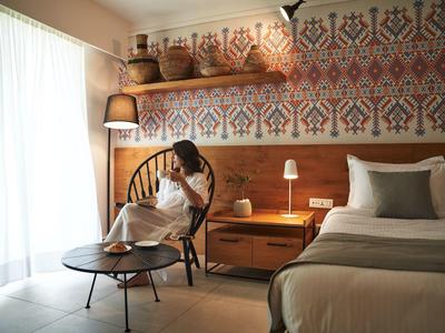 Gästezimmer mit gemusterten Wandfliesen, Holzmöbeln und einer Person im Stuhl am Fenster.