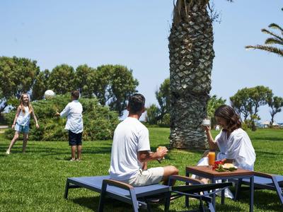 Persone che si rilassano su un prato con palme e tavoli con tempo soleggiato.