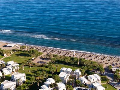 Luftaufnahme eines Strandhotels mit Sonnenschirmen, Liegen und ruhigem Meer im Hintergrund.