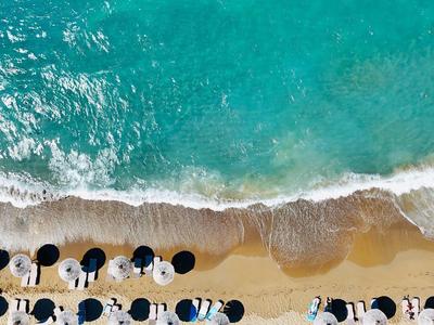 Luchtfoto van een strand met ligbedden, parasols en golven bij de kust.
