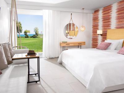 Modernes Hotelzimmer mit Doppelbett, Sofa, Schreibtisch und Blick auf den Garten und Meer.