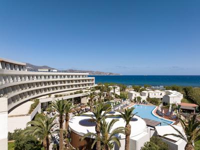 Moderner Hotelkomplex mit Pool und Palmen, Blick auf das blaue Meer unter klarem Himmel.