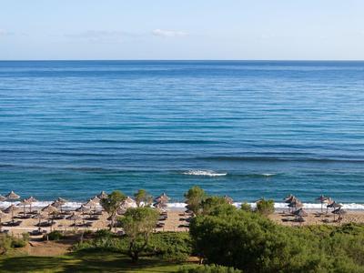Strand mit Sonnenschirmen, Liegestühlen und blauem Meer im Hintergrund bei klarem Himmel.