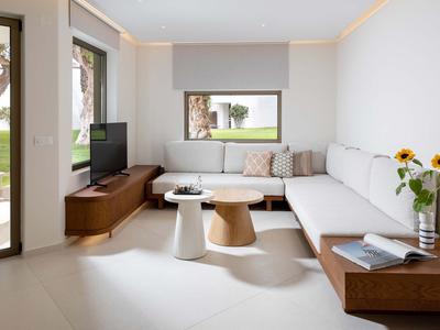 Helles Wohnzimmer mit moderner Einrichtung, Sofas, Couchtischen und Blumendekor in einem Hotelzimmer.